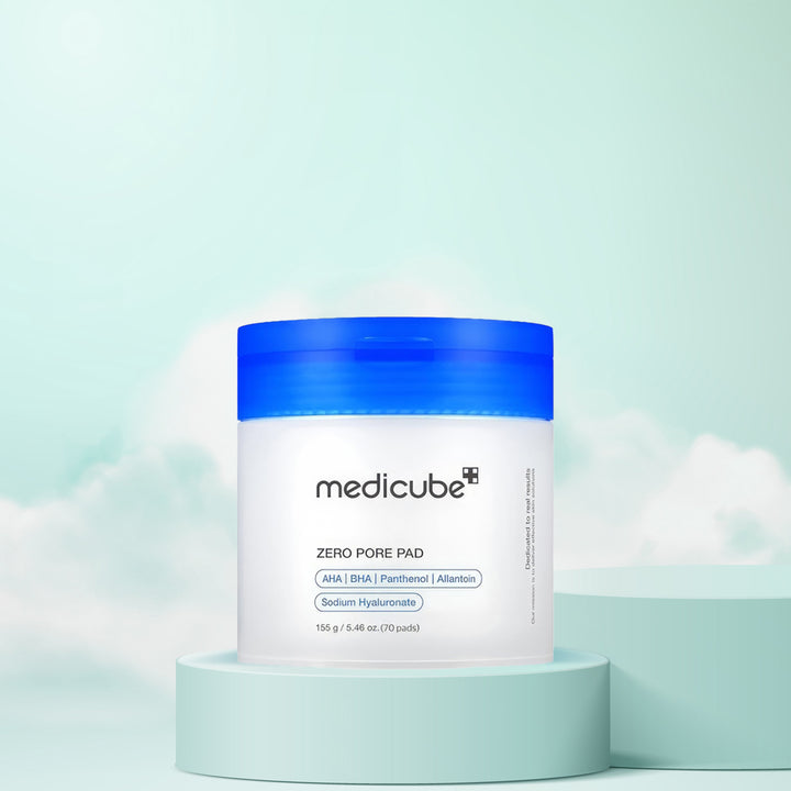 A container of Medicube Zero Pore Pad placed on a pedestal against a blue background with cloud-like patterns.