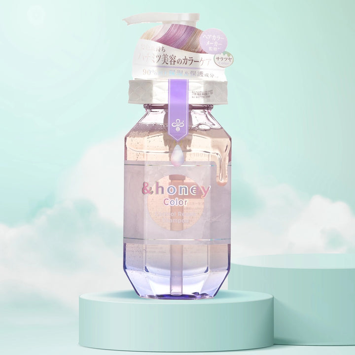 A clear plastic bottle of &Honey Color Control Repair Shampoo by ViCREA with a purple cap, displayed against a pastel background with a cloud-like design.