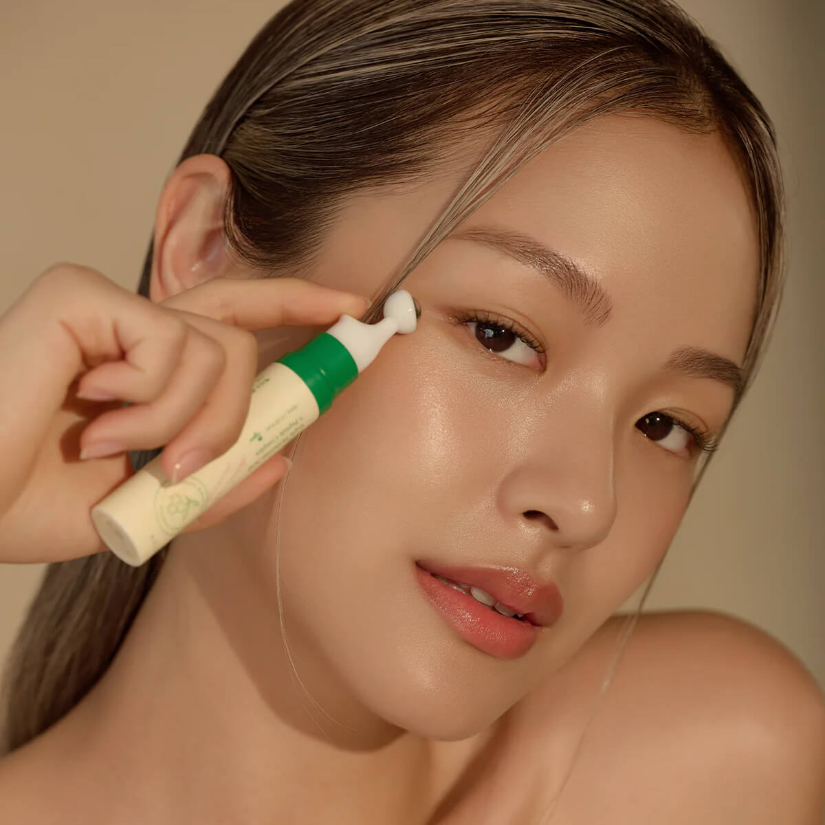 Person applying makeup with a brush to their face against a neutral background