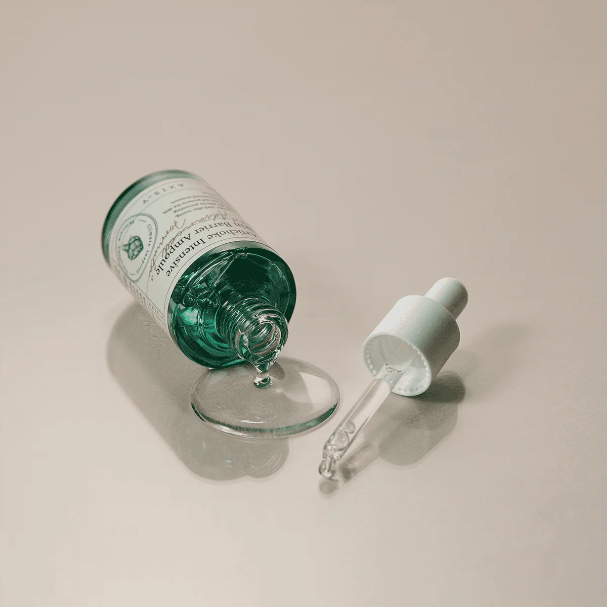 Green glass dropper bottle with a white cap on a beige background