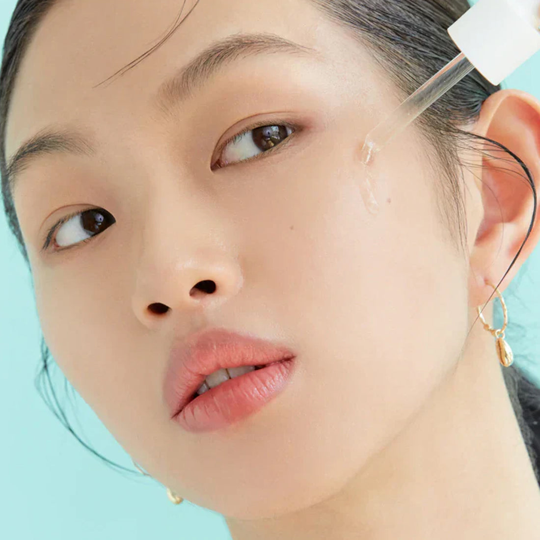 Close-up of a person wearing gold hoop earrings against a light blue background