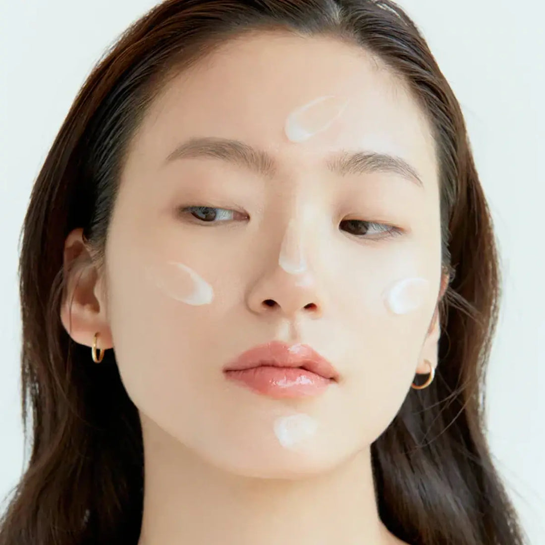 Woman with cosmetic products on her face against a white background