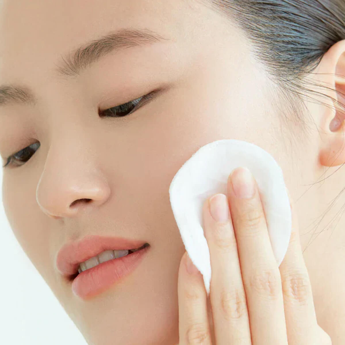Person using a white cotton pad on their face