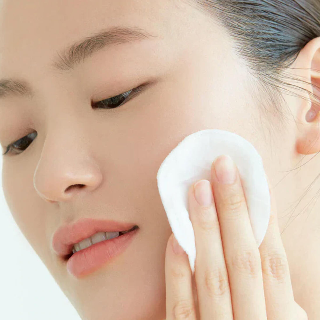 Person using a white cotton pad on their face