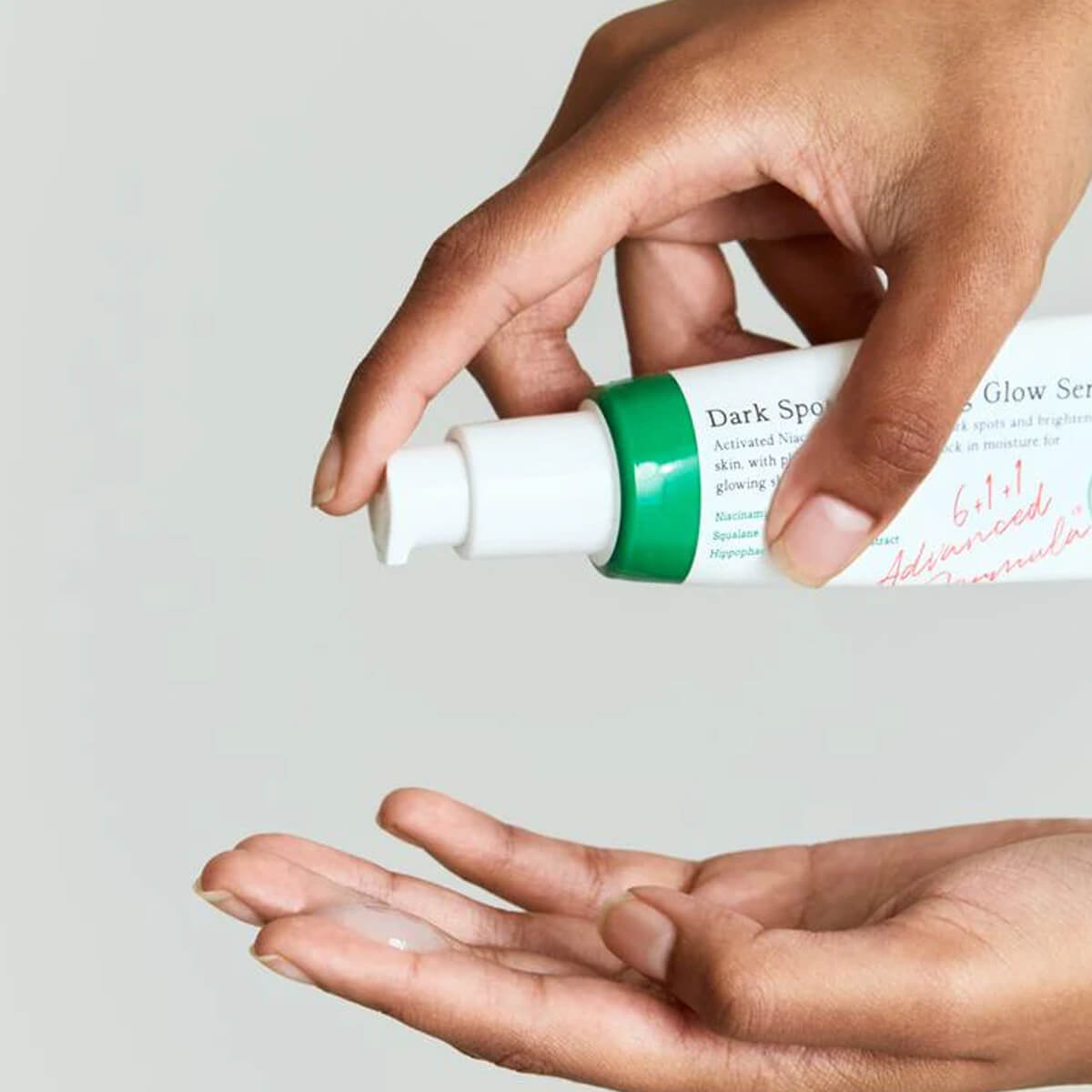 Hand holding a skincare serum bottle with a gray background