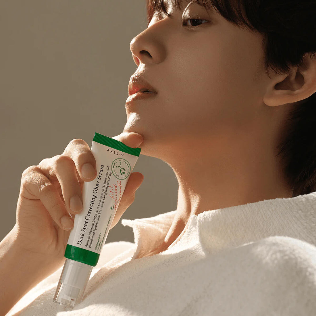 Person holding a skincare serum tube with a neutral background