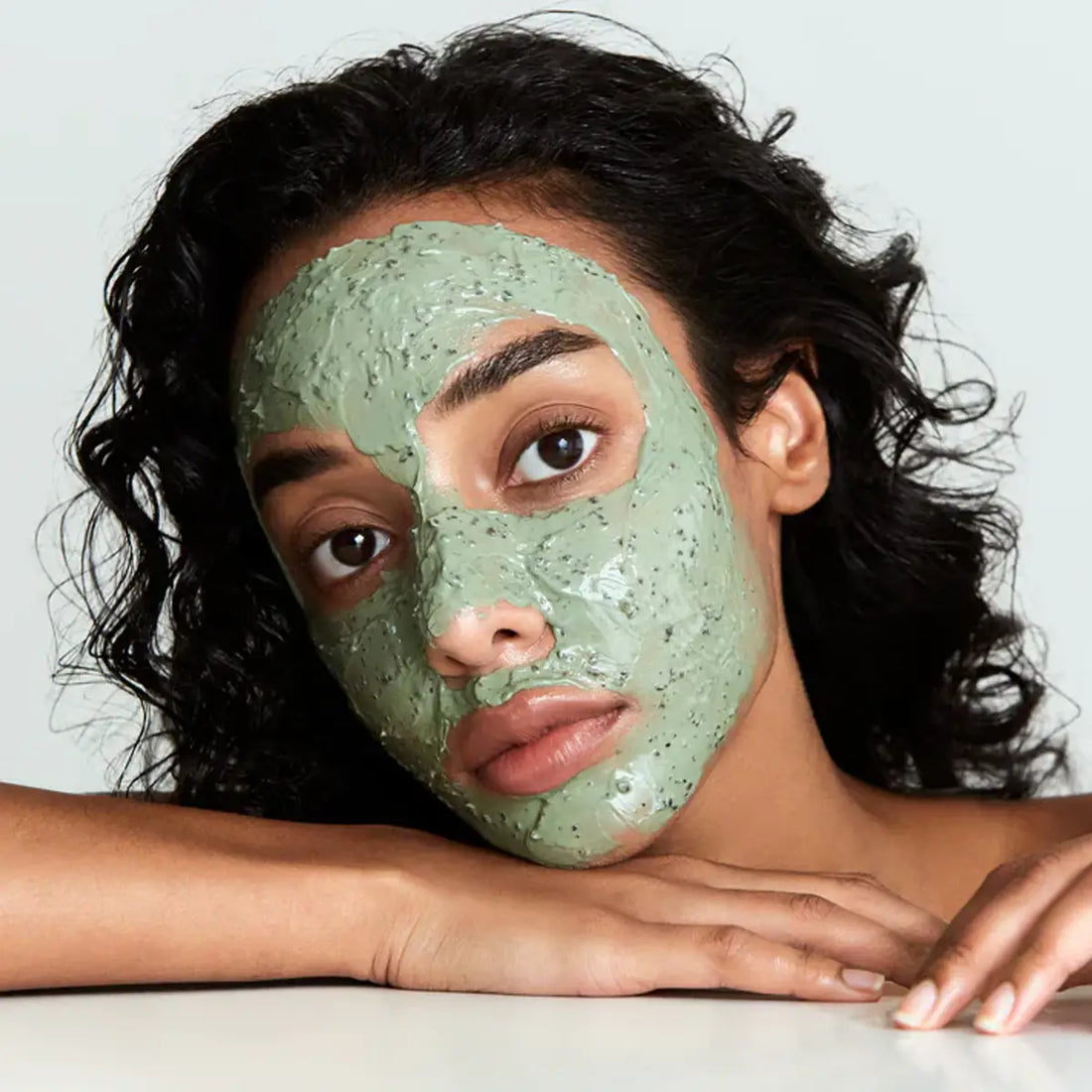 Woman with a green facial mask on her face against a plain background