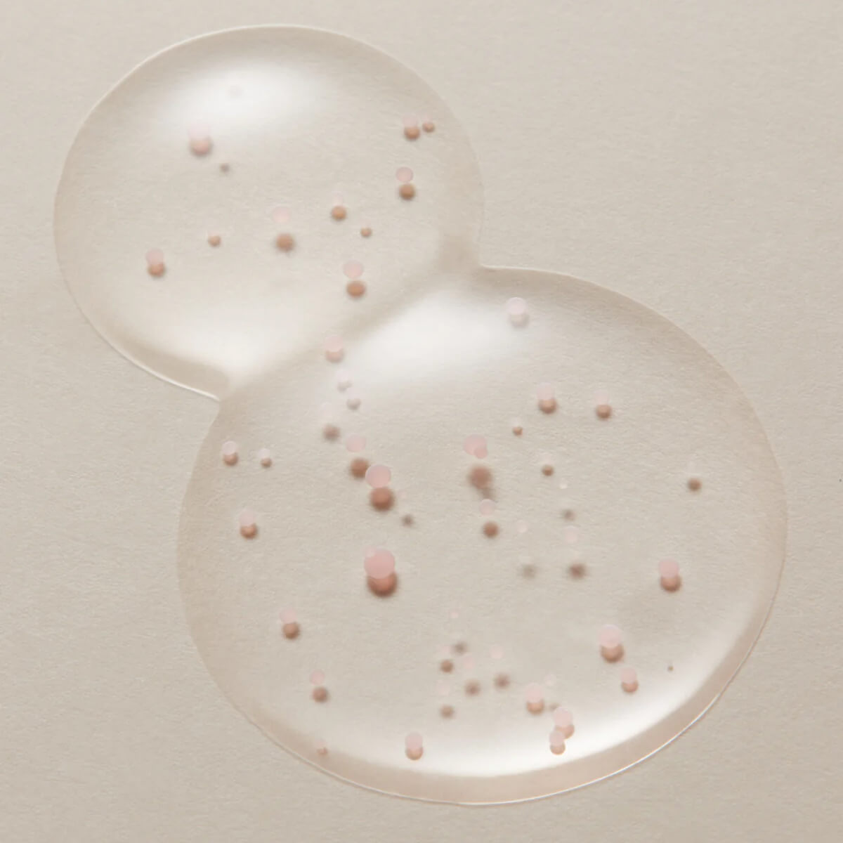 Two clear bubbles with pink and white spherical particles on a light beige background