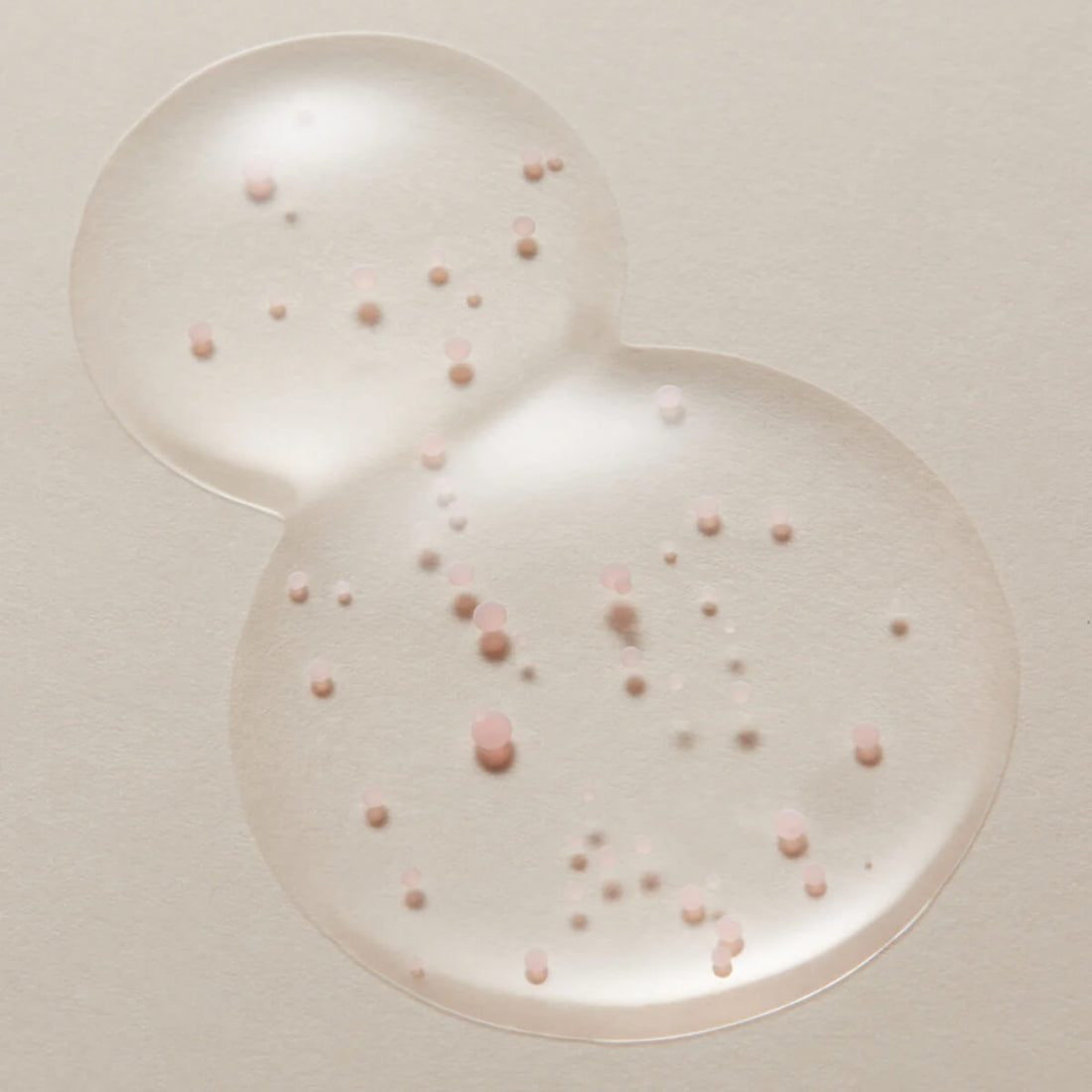 Two clear bubbles with pink and white spherical particles on a light beige background