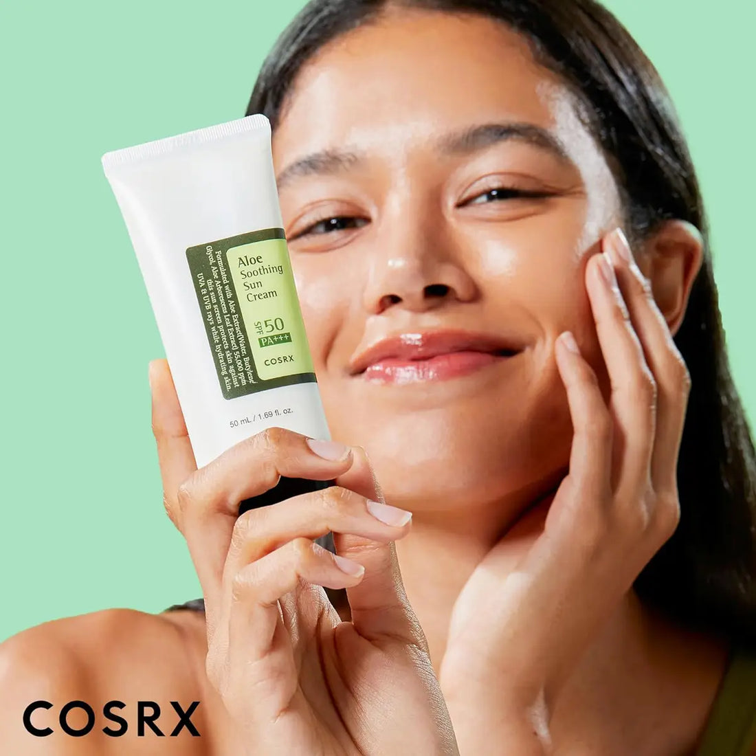Woman applying sunscreen cream with a green background, featuring the COSRX brand.