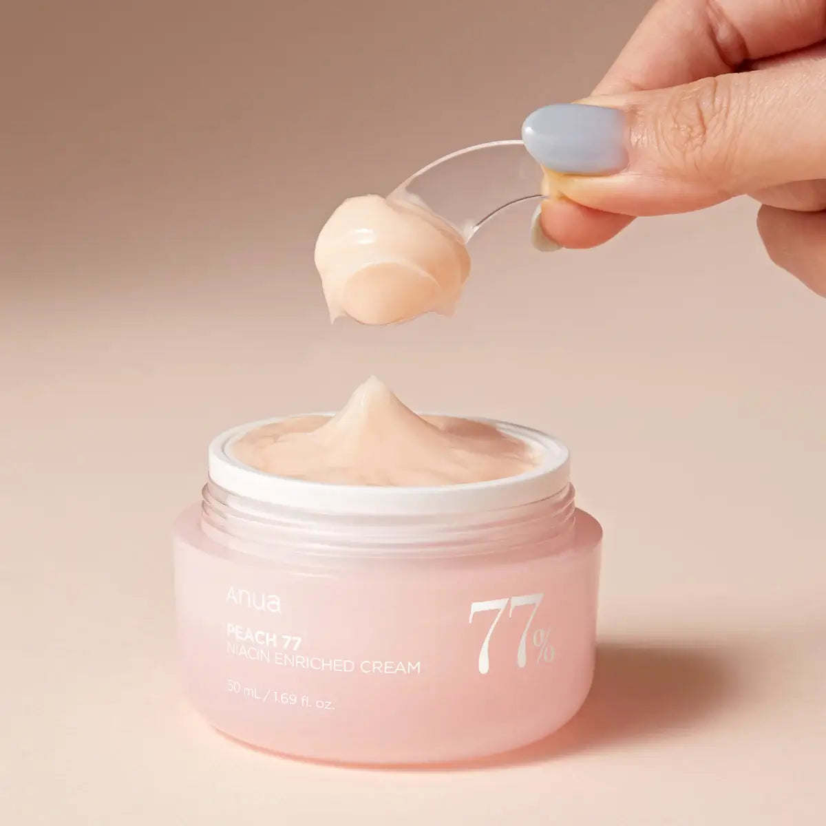 Pink jar of cream with a hand using a spoon to scoop out some cream against a beige background