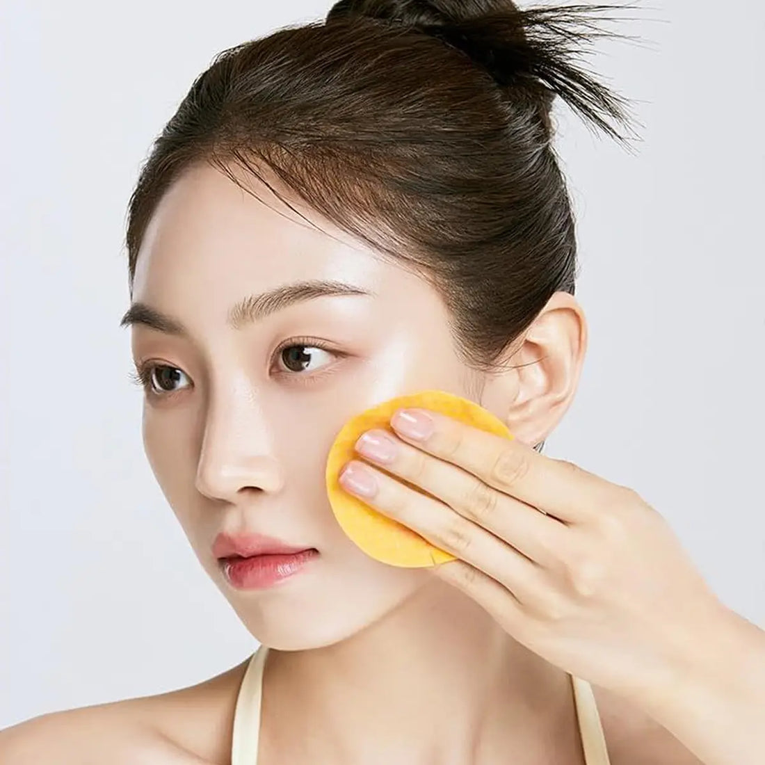Woman applying a yellow facial pad to her face against a white background