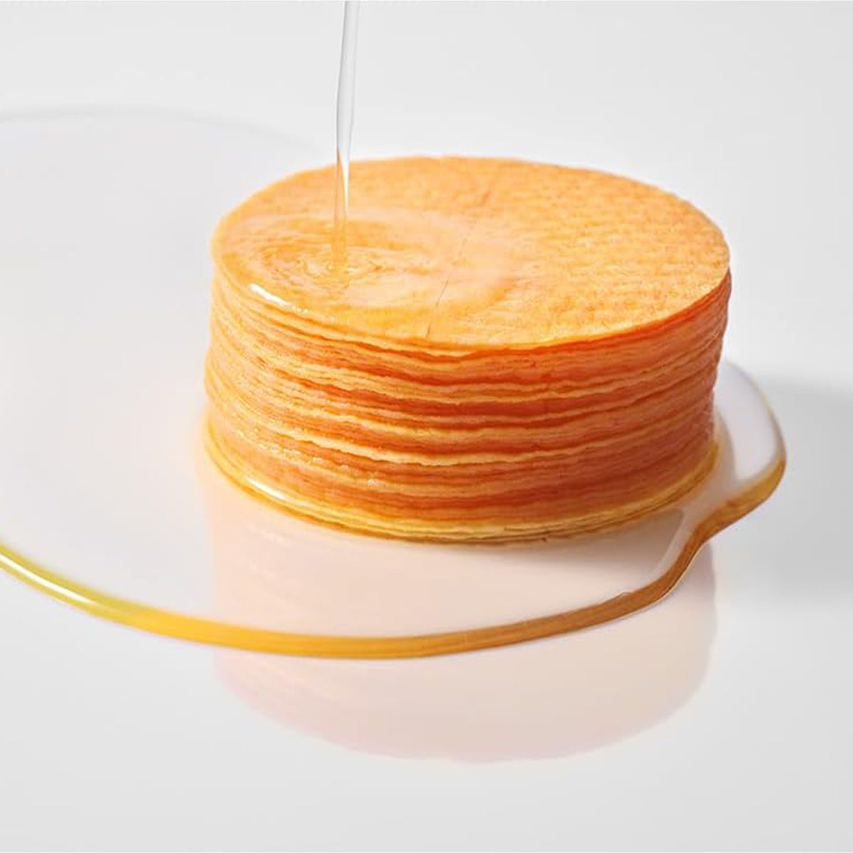 Stack of thin pancakes on a white plate with a white background