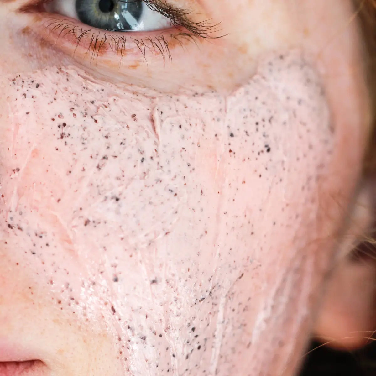 Close-up of a person's face with a pink scrub on their skin