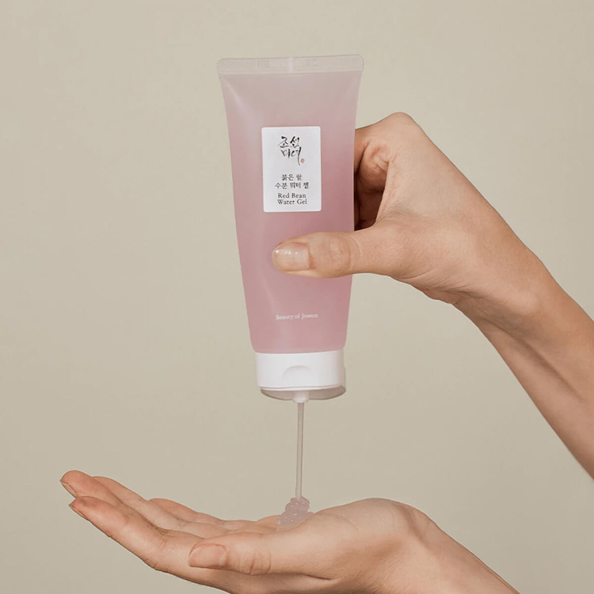 Hand holding a pink tube of skincare product with a beige background