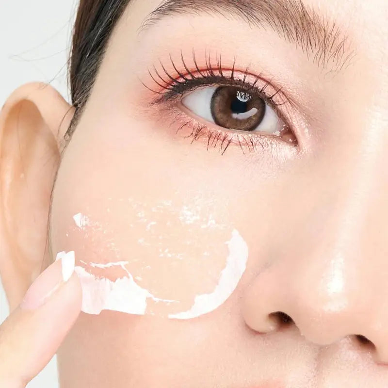 Close-up of a person applying brightening cream to their face with a neutral background