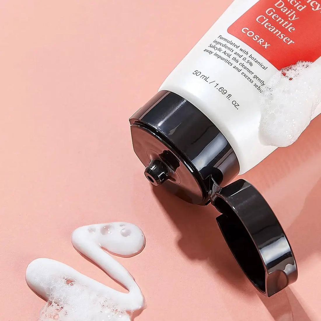 Cosrx Daily Gentle Cleanser tube with foam on a pink background