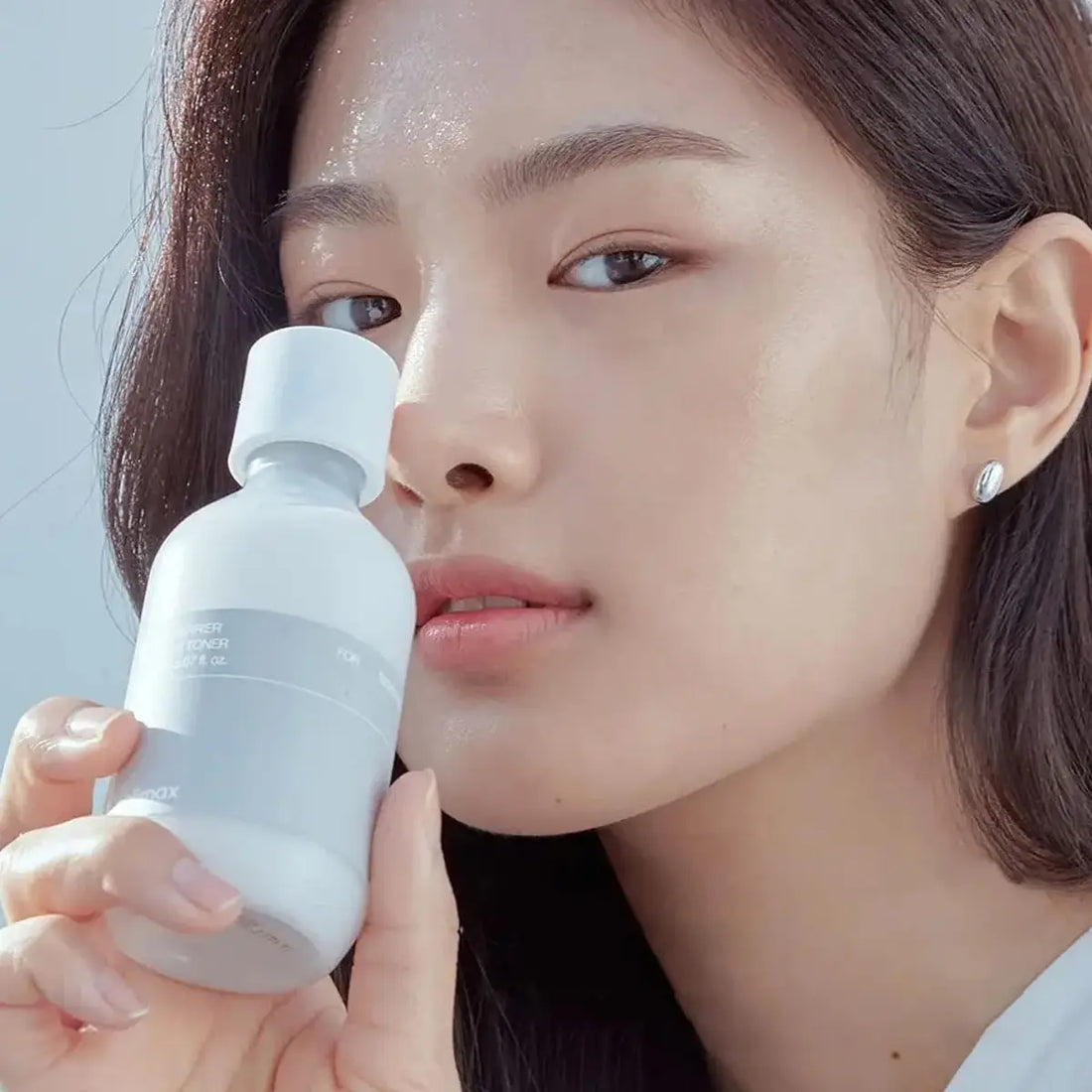 Woman holding a Celimax Dual Barrier Creamy Toner close to her face against a light background