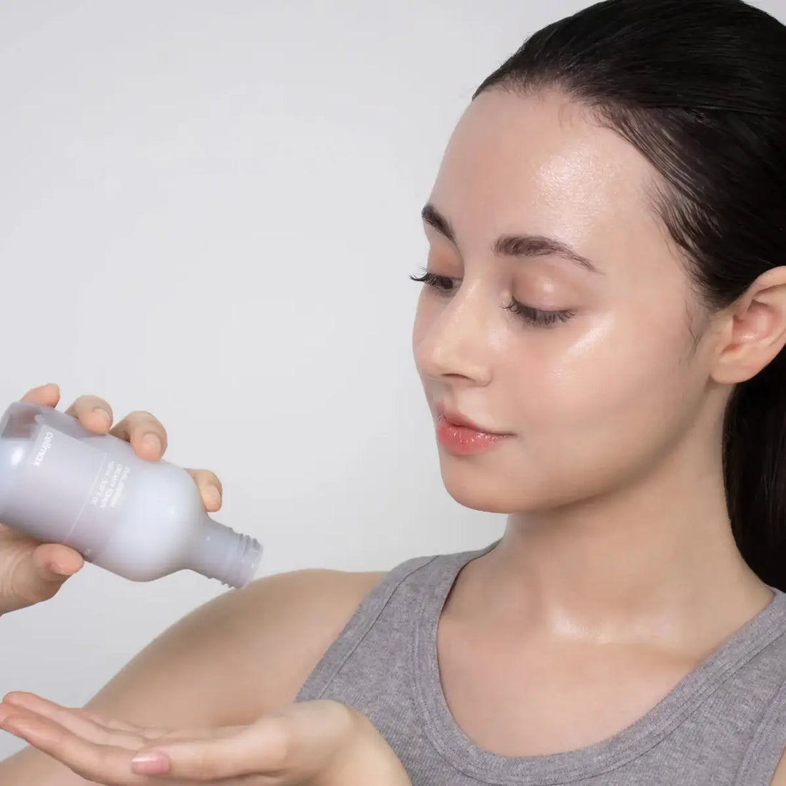 Woman applying aCelimax Dual Barrier Creamy Toner to her arm against a plain background