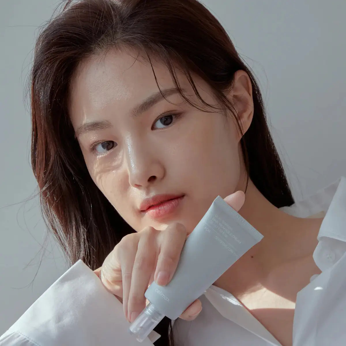 Woman holding a Celimax Dual Barrier Skin Wearable Cream against a neutral background
