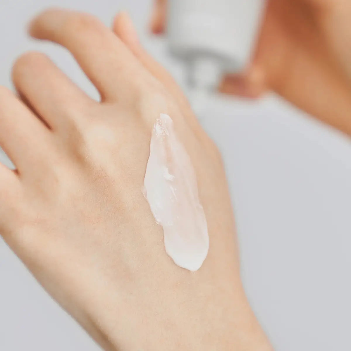 Hand with a small amount of cream on the palm against a neutral background