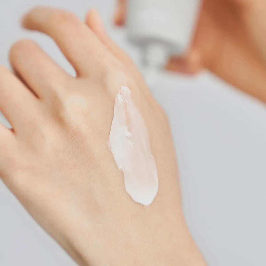 Hand with a small amount of cream on the palm against a neutral background
