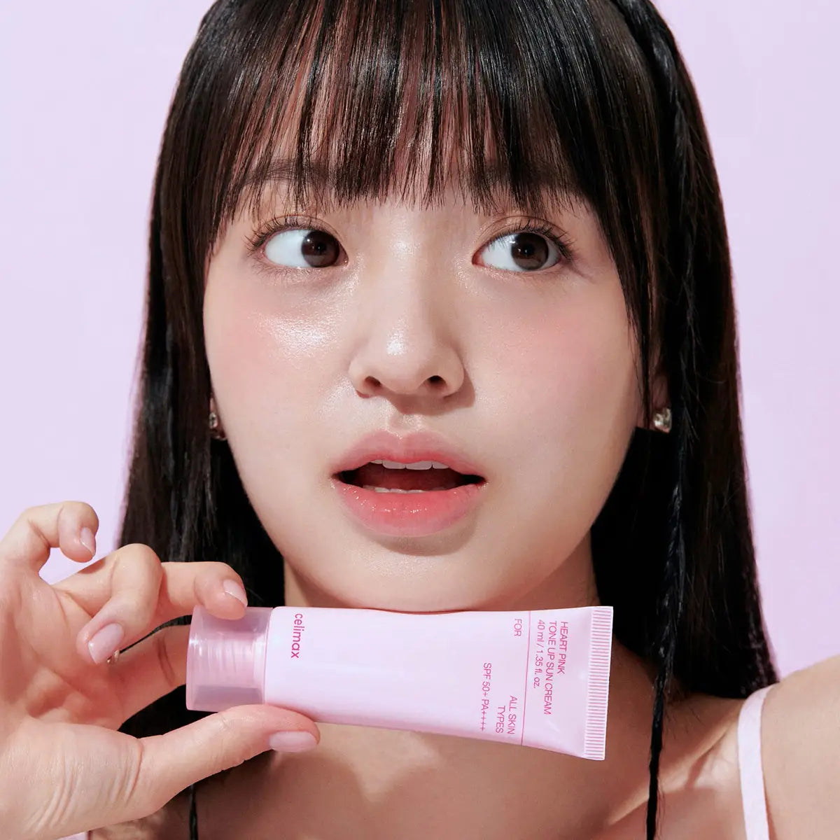 Woman holding a pink Celimax sunscreen product against a light purple background