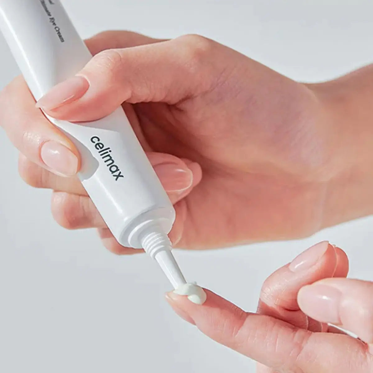 Hand applying Celimax Noni Ultimate Eye Cream on a light background