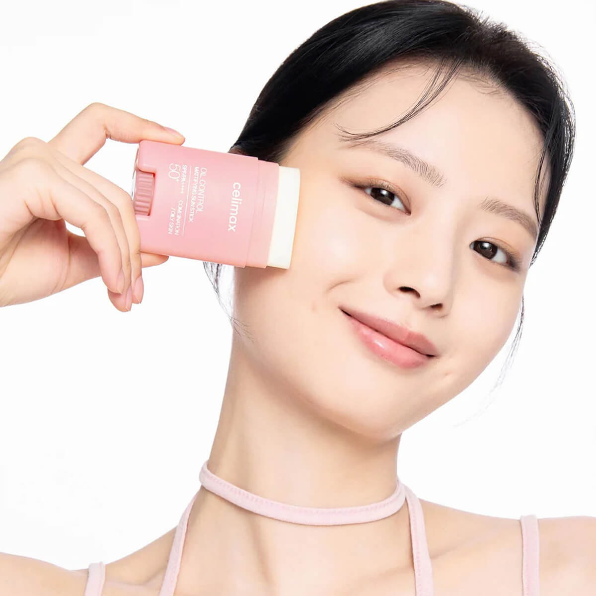 Woman holding a pink skincare product against her face on a white background