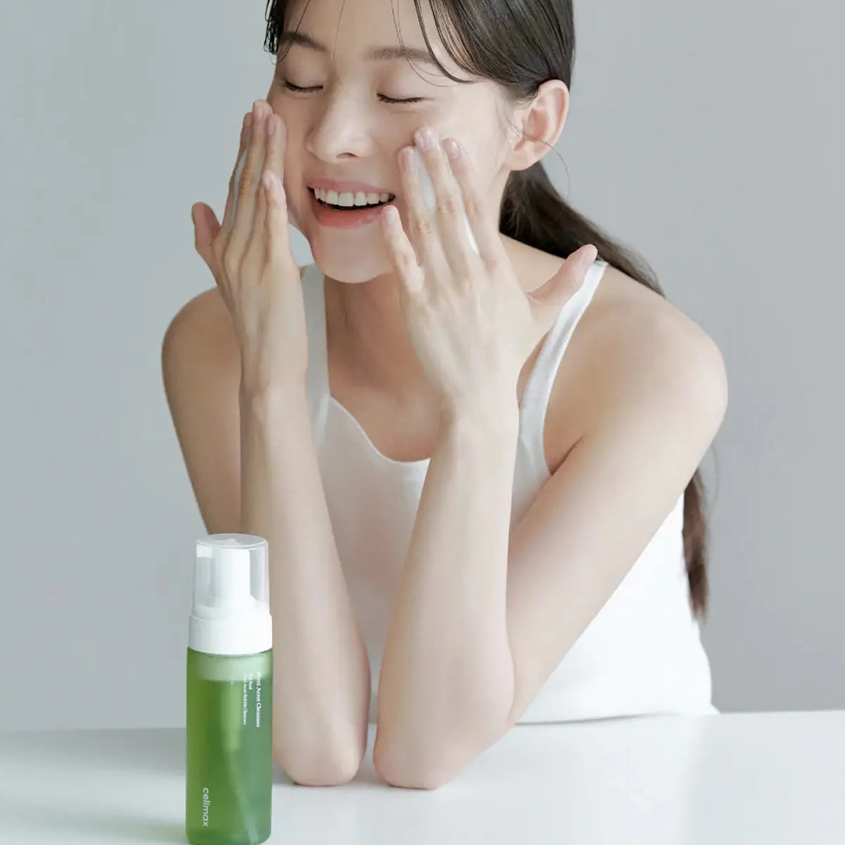 Woman applying cream to her face with a green skincare bottle in front of her.