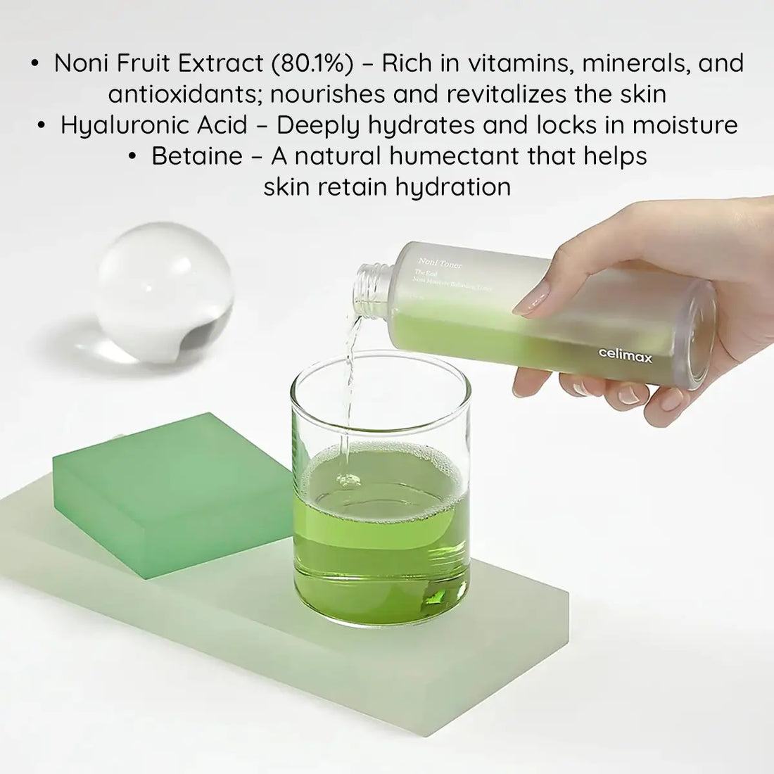 Hand pouring green liquid from a bottle labeled 'celimax' into a glass, with product details about Noni Fruit Extract and Hyaluronic Acid on a white background.