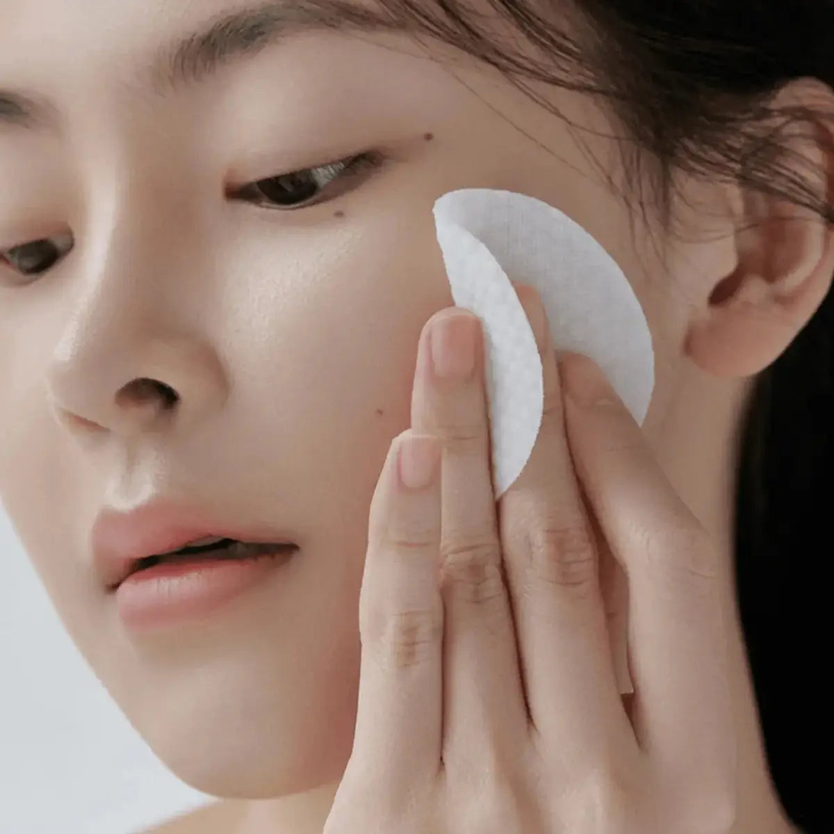 Person using a Celimax Ji Woo Gae Heartleaf BHA Peeling Pad on their face against a neutral background