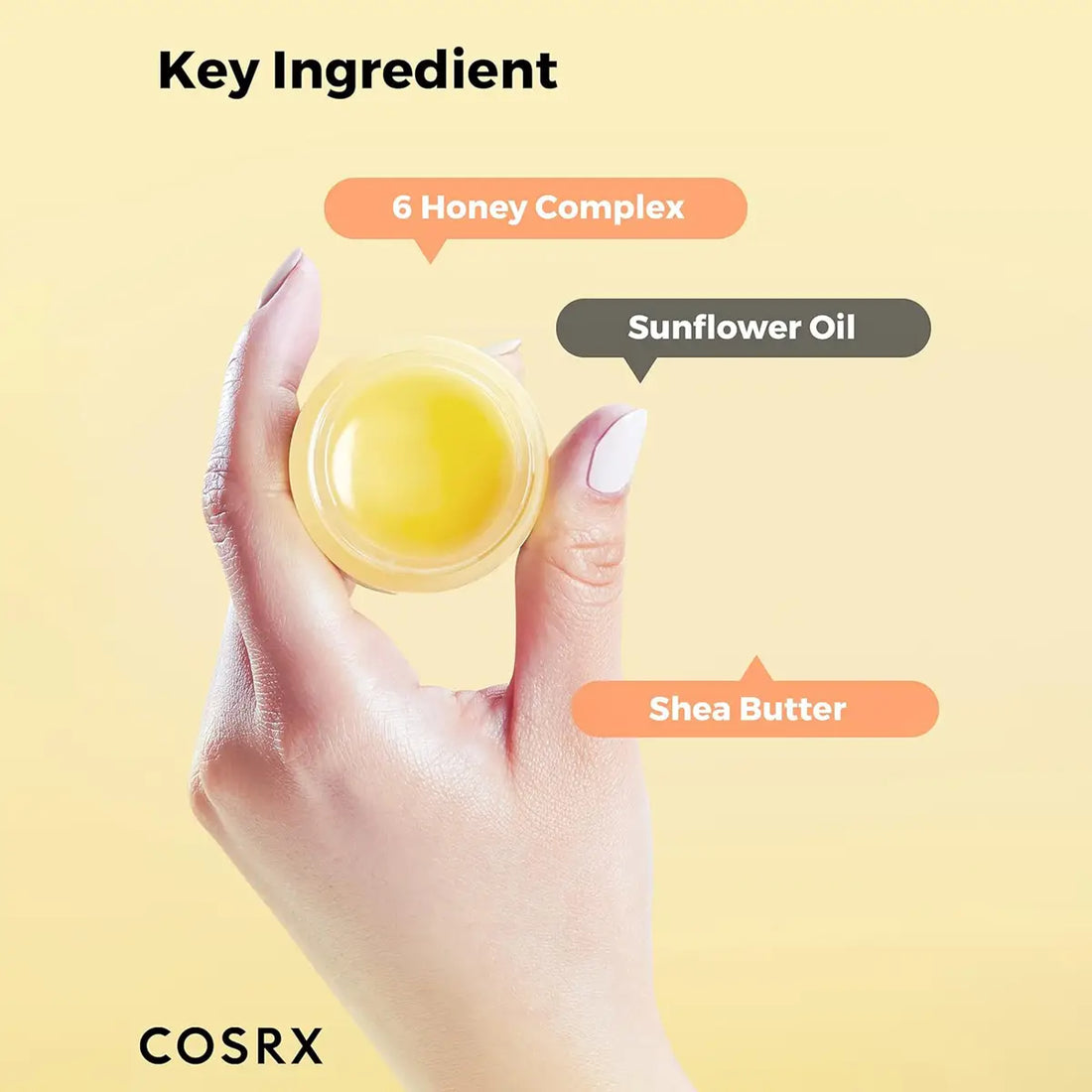 Hand holding a yellow lip balm with labeled ingredients on a yellow background, featuring the COSRX brand.