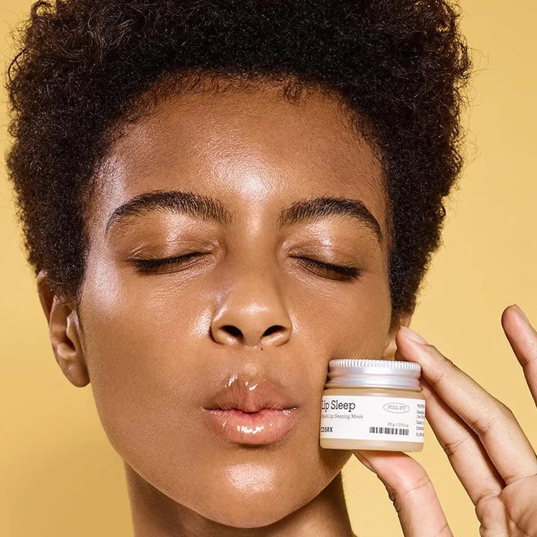 Person holding a jar of 'Lip Sleep' against a yellow background