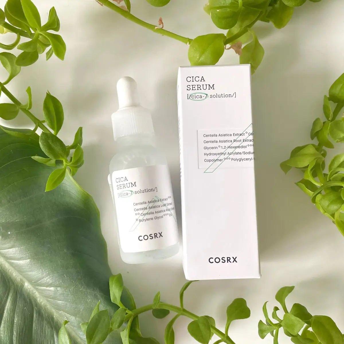 COSRX Cica Serum bottle and packaging on a light background with green leaves.