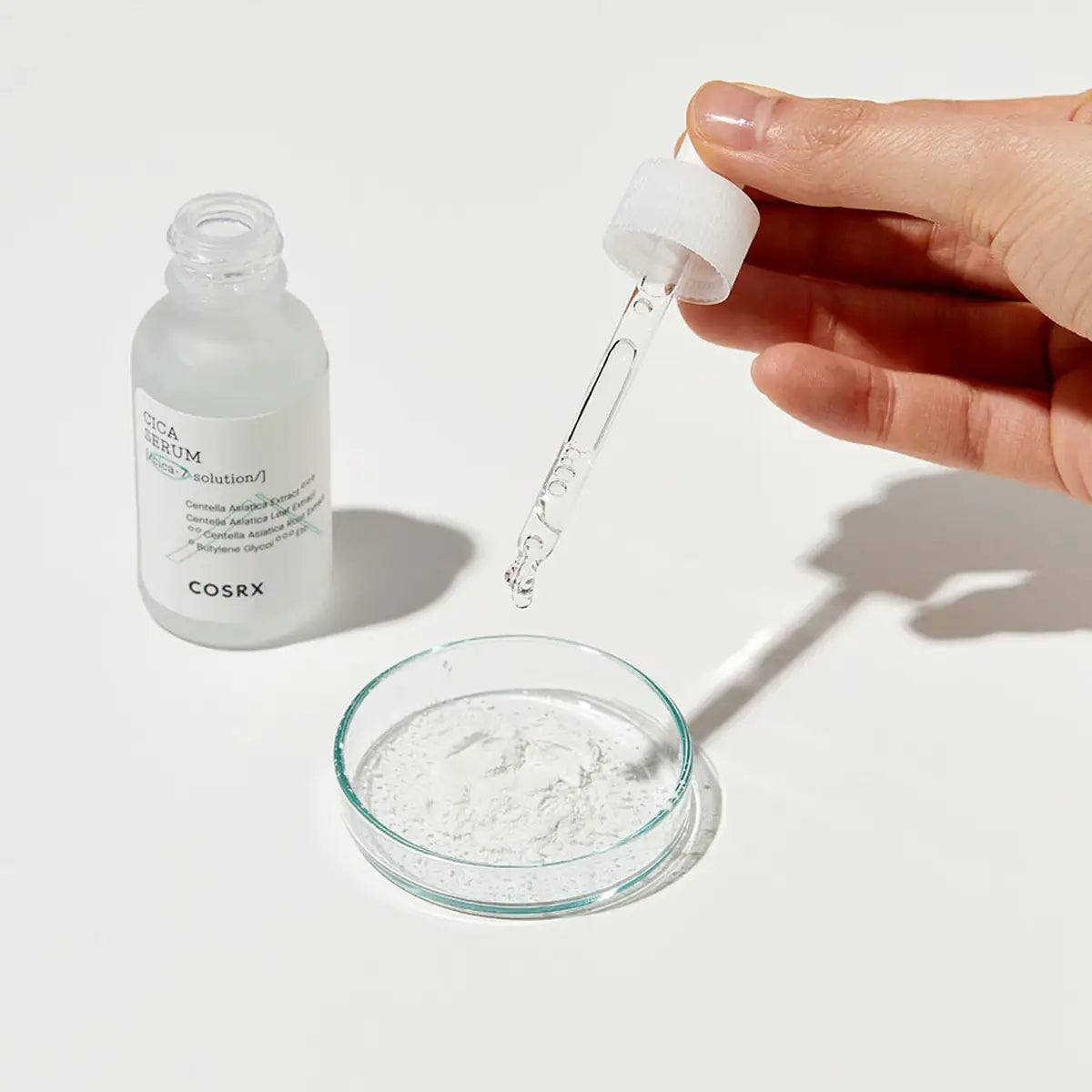 Cosrx serum bottle with dropper and glass dish on a white background