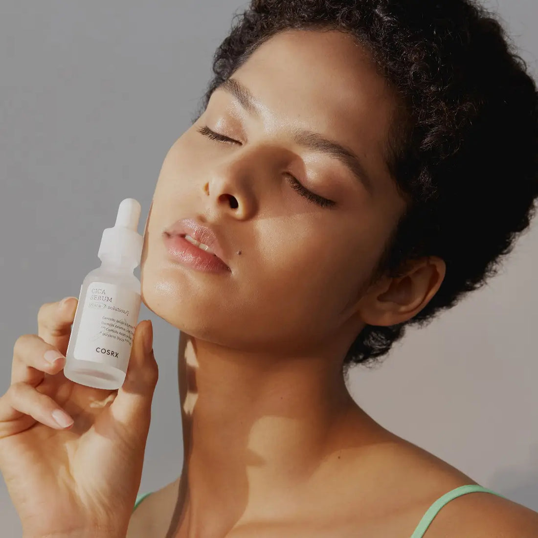 Woman holding a Cosrx dropper bottle against a neutral background