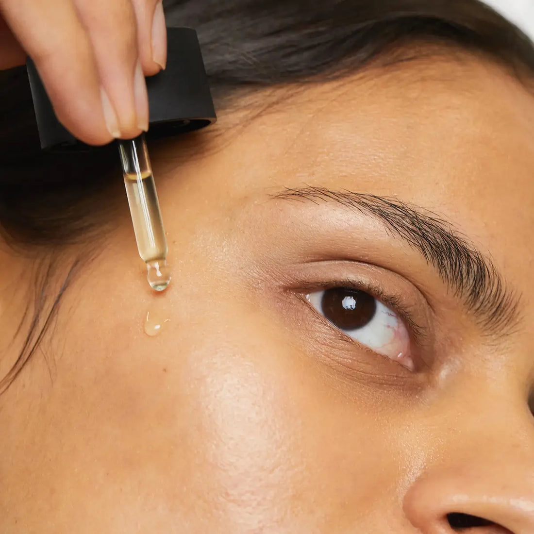 Person applying a dropper of liquid to their face