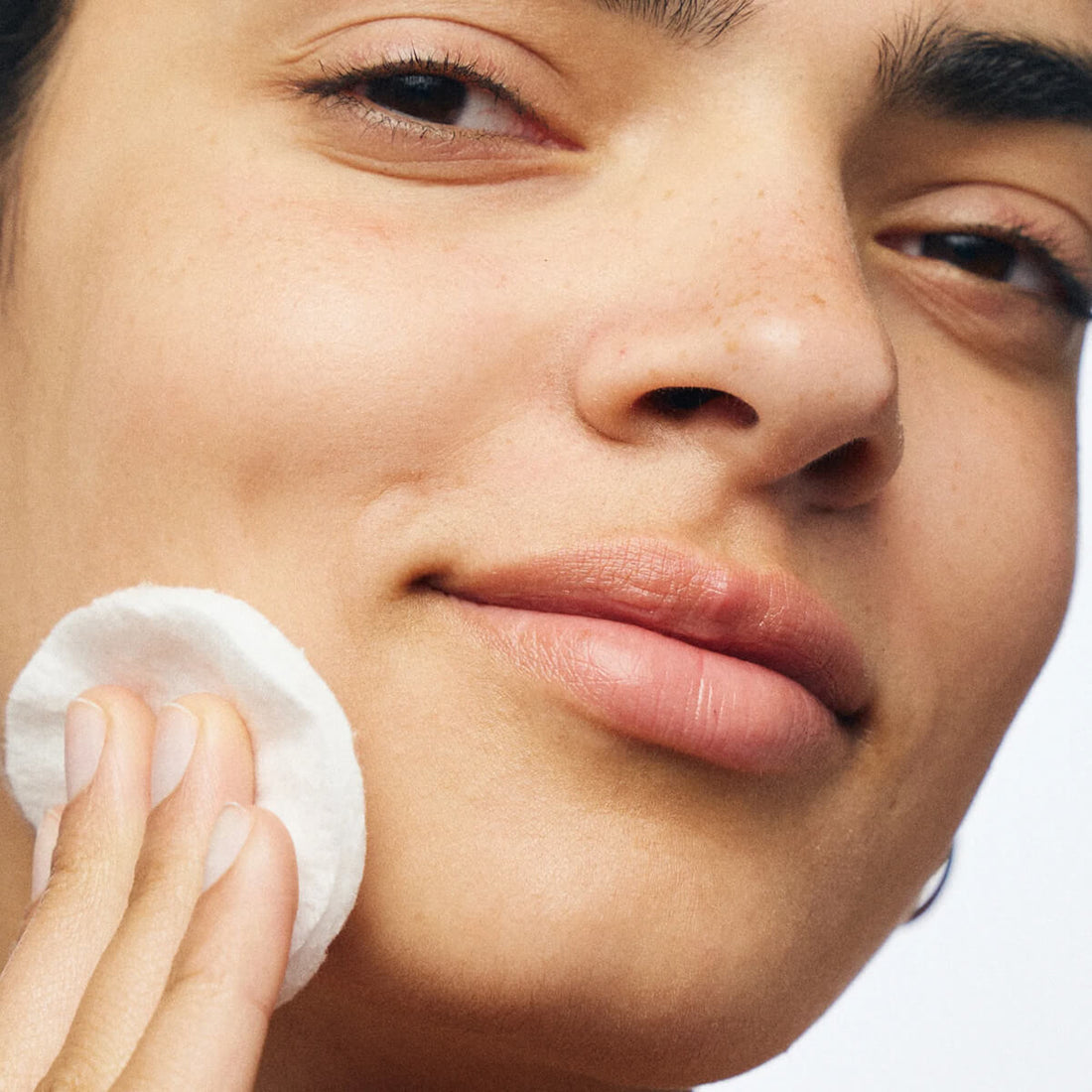 Close-up of a person using a cotton pad on their face.