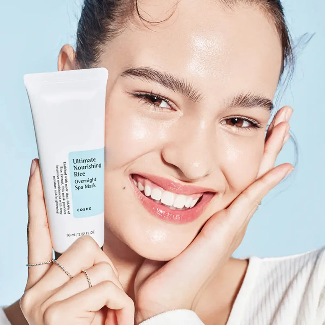 Woman holding a Cosrx skincare product against a light blue background