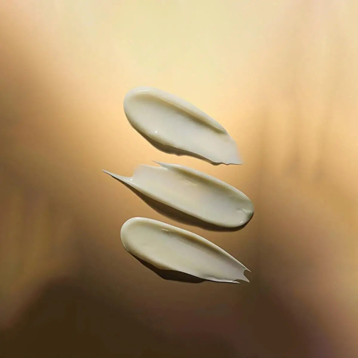 Three swatches of cream on a gradient gold background