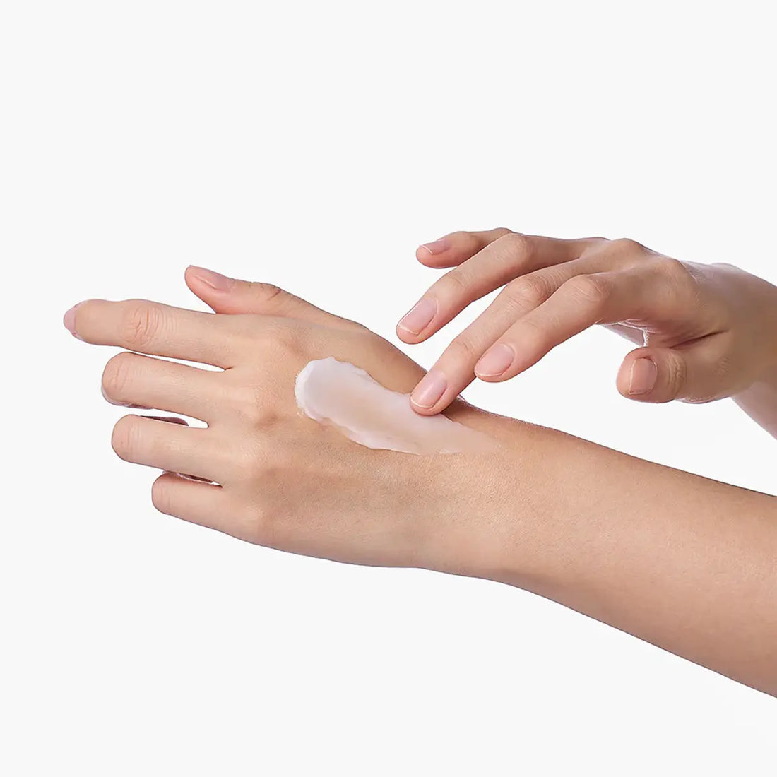 Person applying a small amount of cream to their hand on a white background