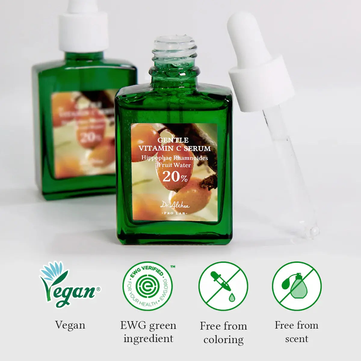 Green serum bottle with labels indicating vegan, EWG green ingredient, free from coloring, and free from scent on a white background.