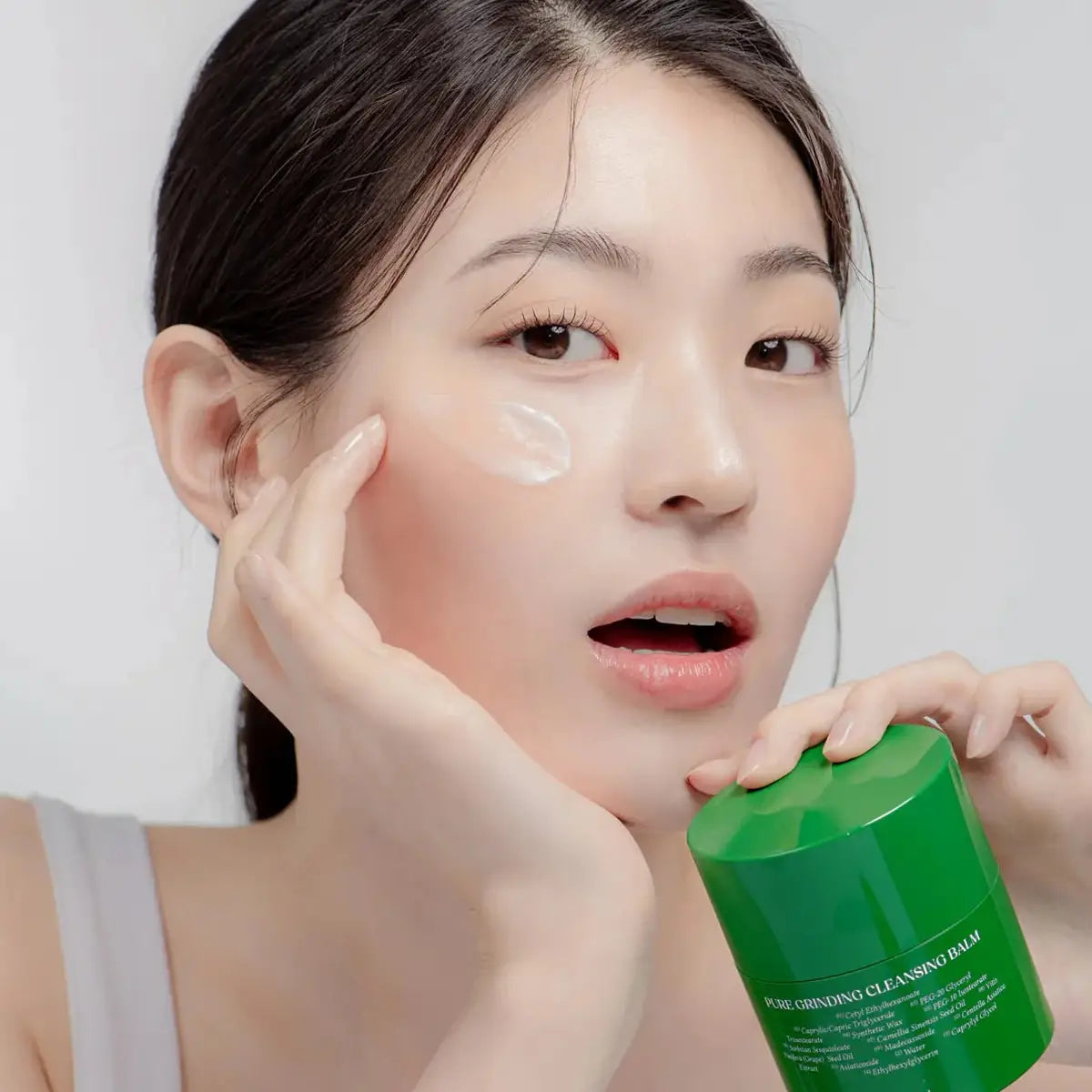 Woman applying cleanser to her face with a green skincare product container.