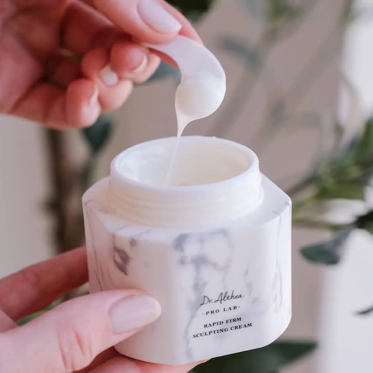 Person applying cream from a jar labeled 'Dr. Althea' with a blurred natural background