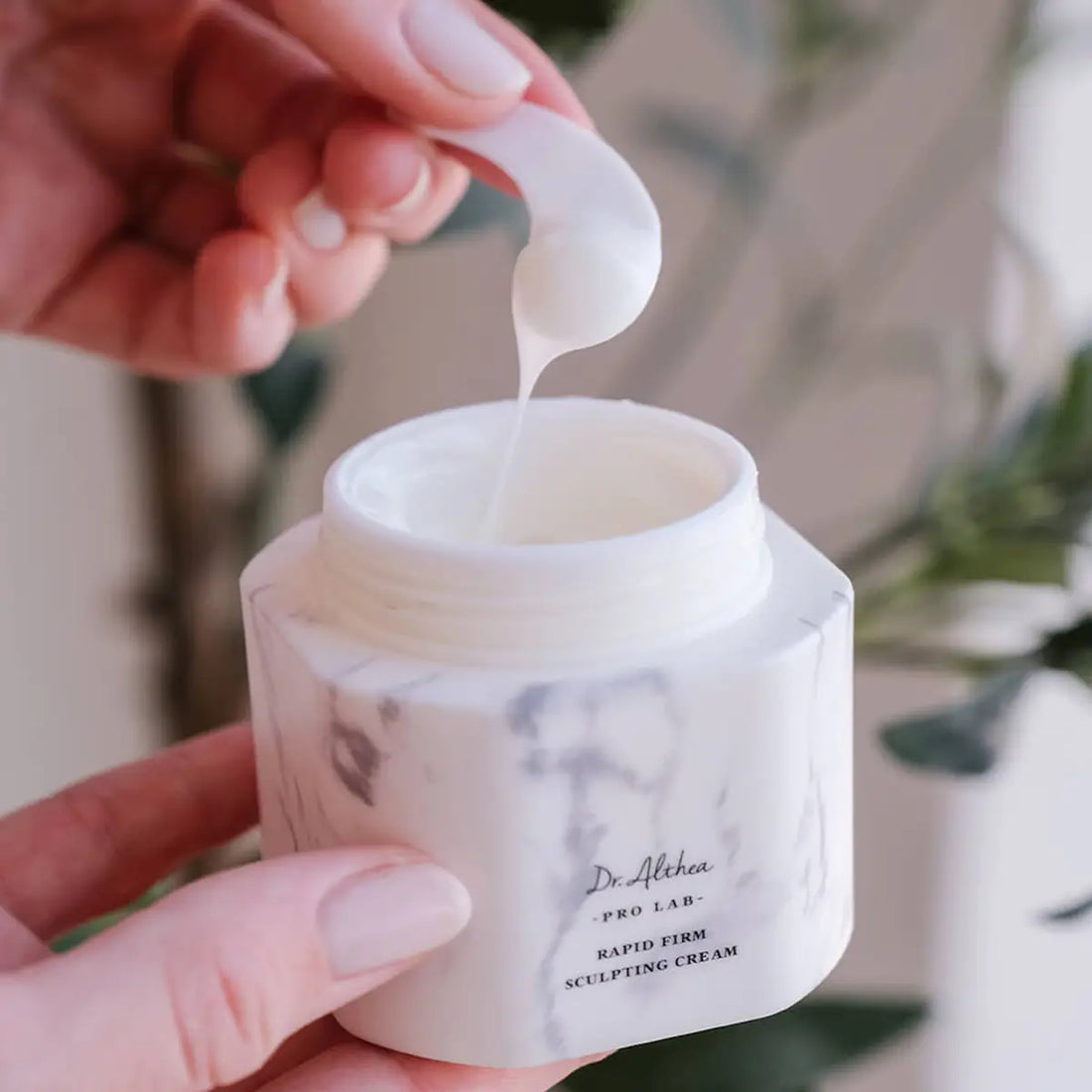 Person applying cream from a jar labeled 'Dr. Althea' with a blurred natural background