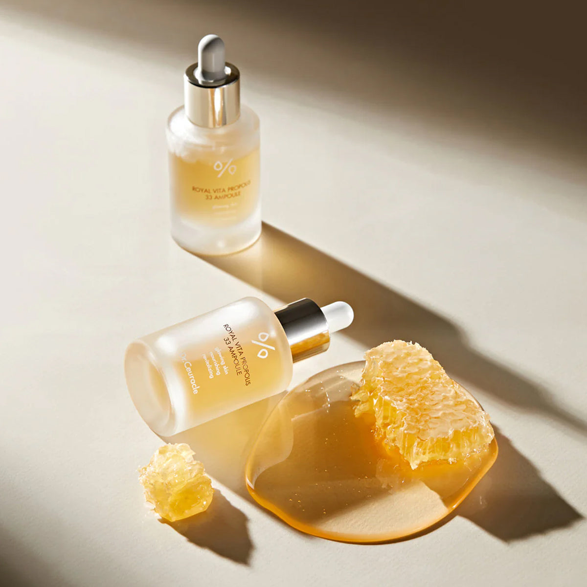 Two skincare serum bottles with a dropper on a beige surface, accompanied by a piece of fruit.
