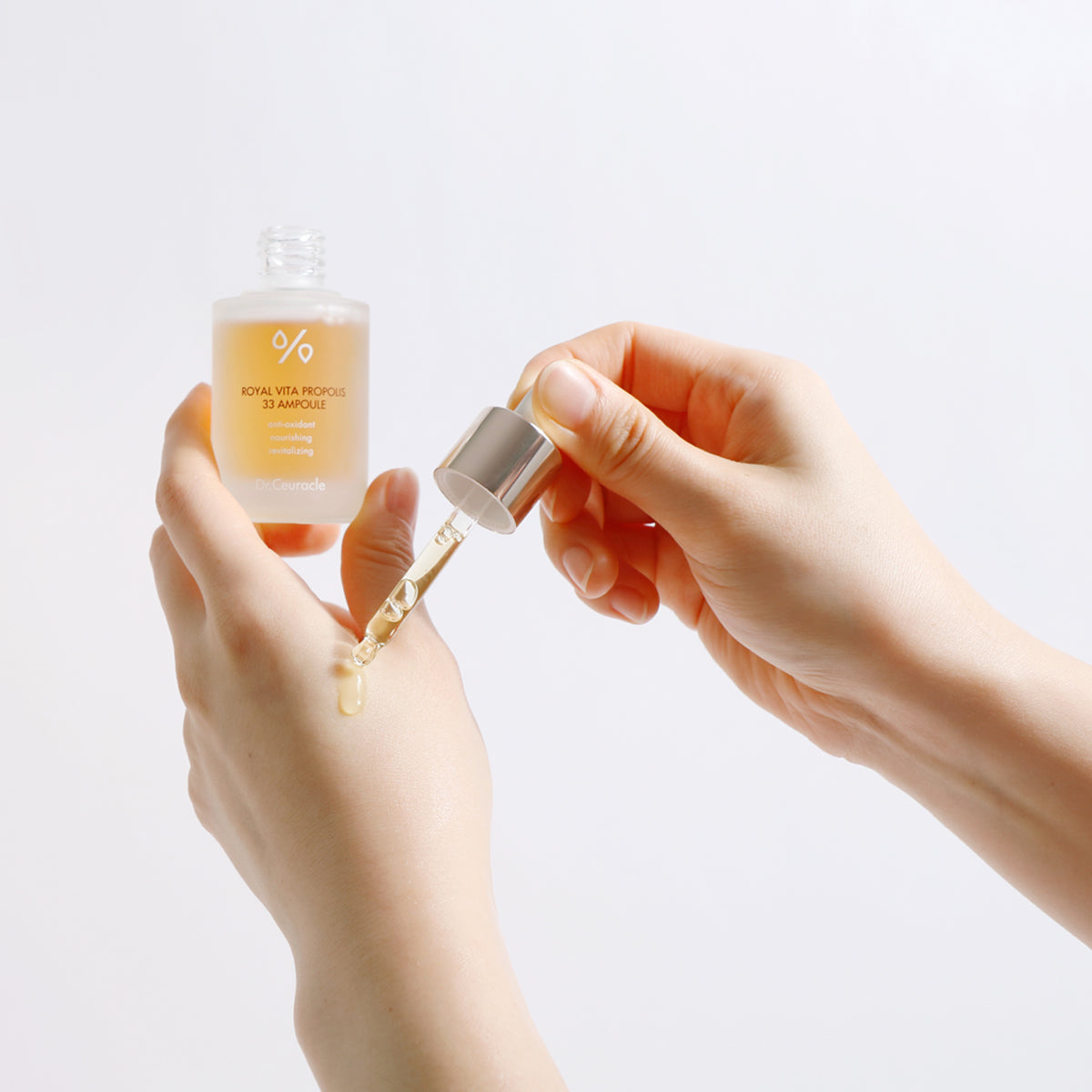 Hand holding a skincare ampoule with dropper on a light background