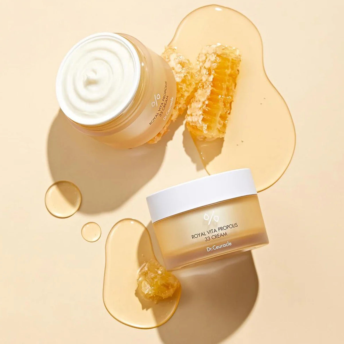 Two jars of cream with a honeycomb and honey on a beige background