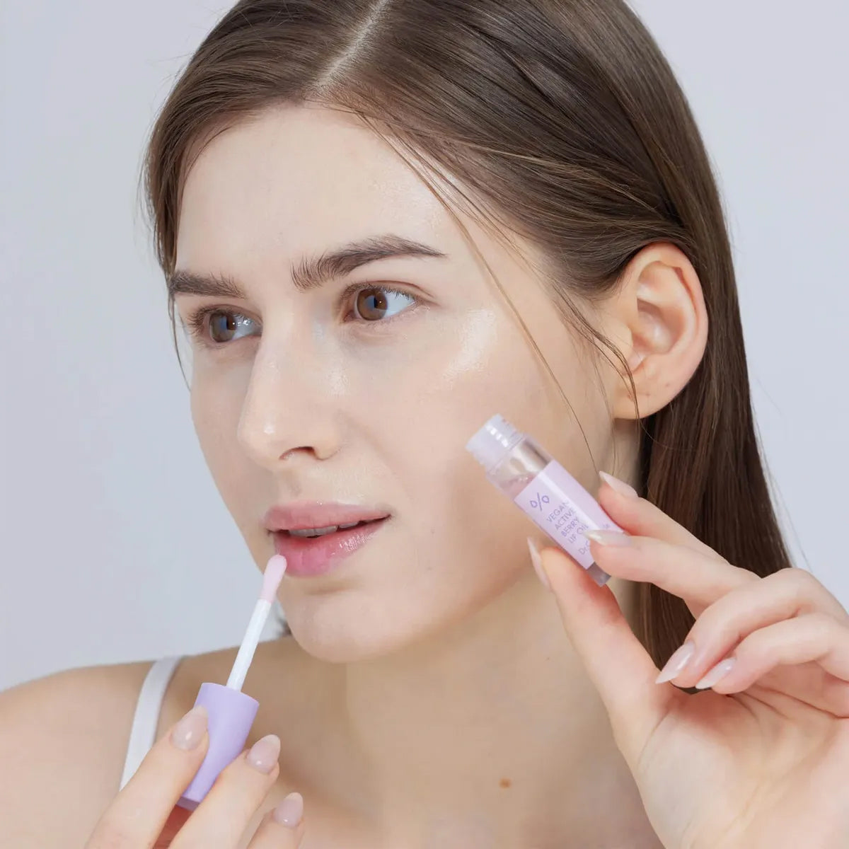 Woman applying a purple lip balm to her lips against a plain background